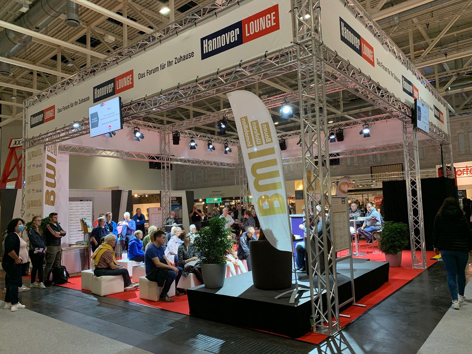 A man and a woman sit on a podium in Radio Hannover&#39;s Hannover Lounge. Spectators sit in front and listen
