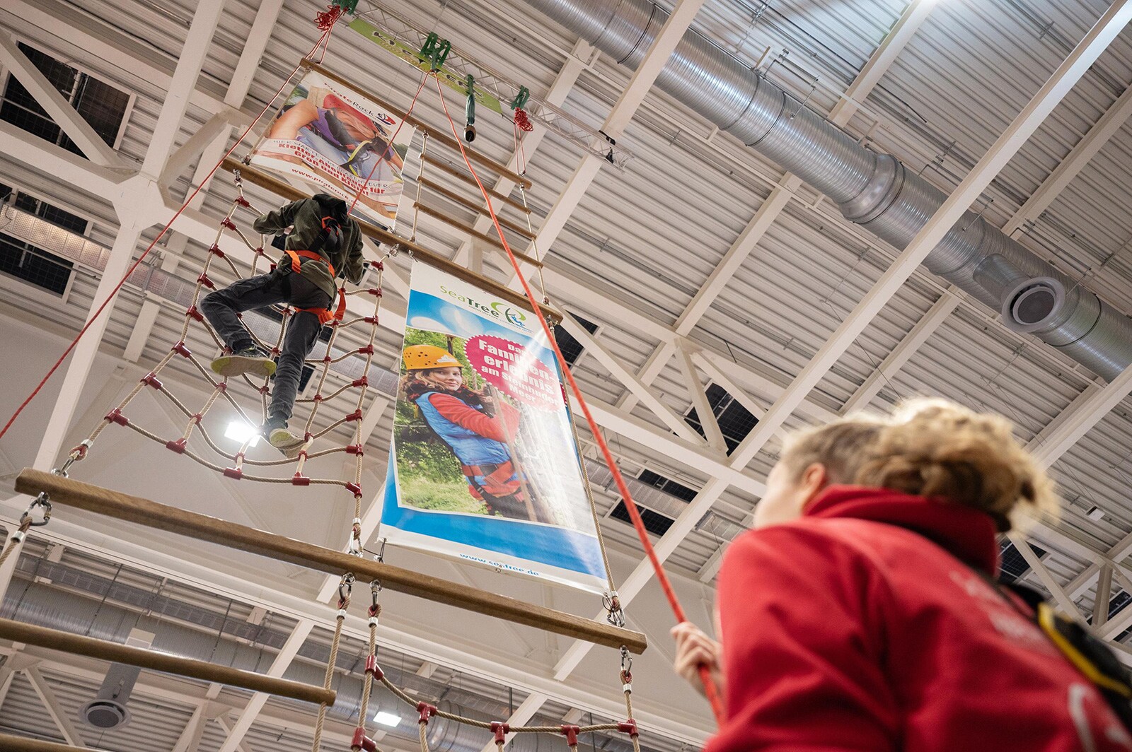 A teenager climbs up a rope course and is secured by a staff member.