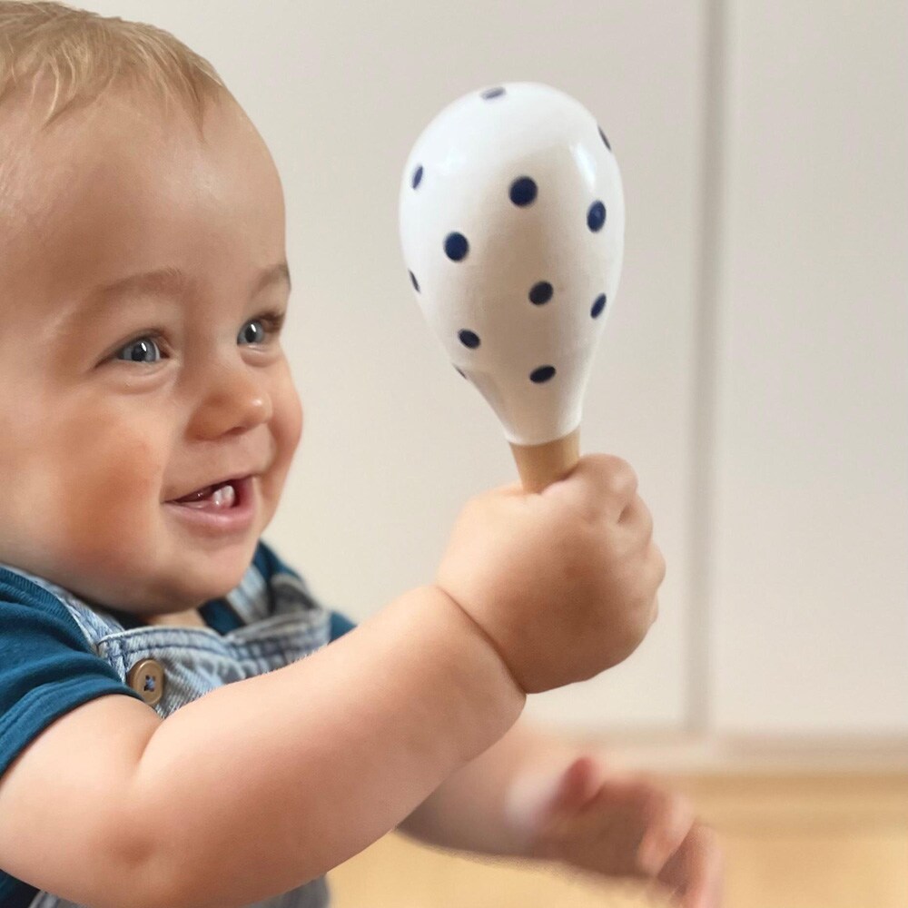 A baby holds a white rattle with black dots in its hand and laughs.