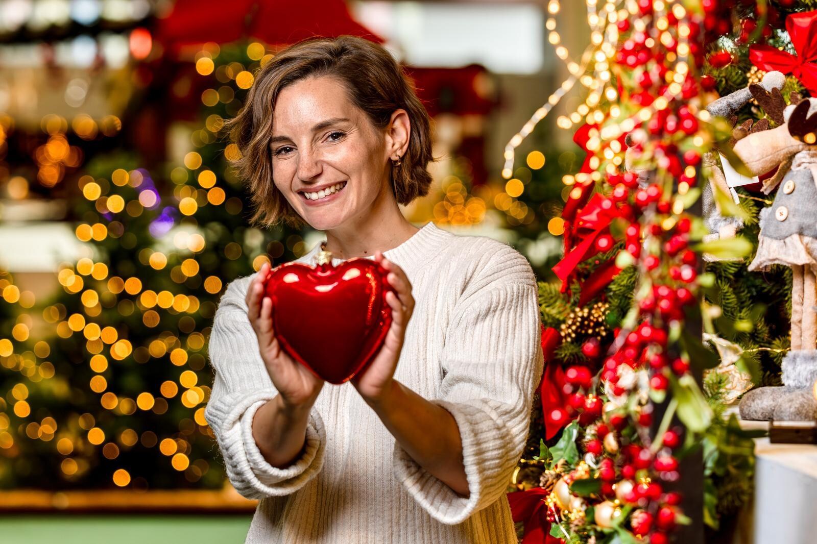 Eine junge Frau hält eine Christbaumkugel in der Hand und lächelt in die Kamera