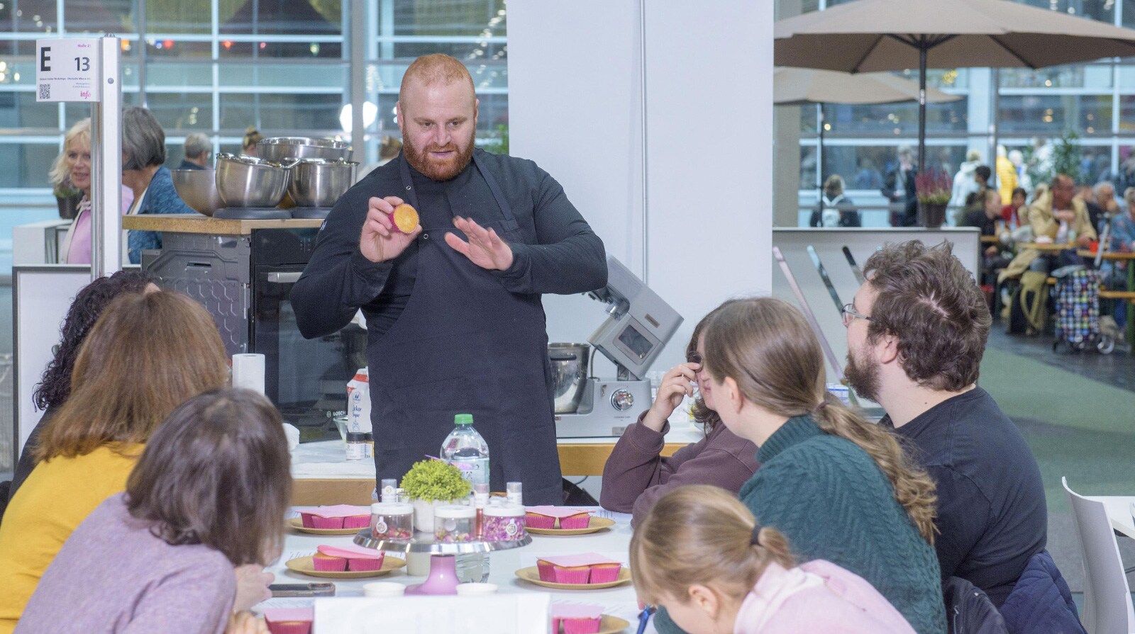 Raheem Haidar steht vor Teilnehmern seines Cupcake Workshops und zeigt ein Produkt