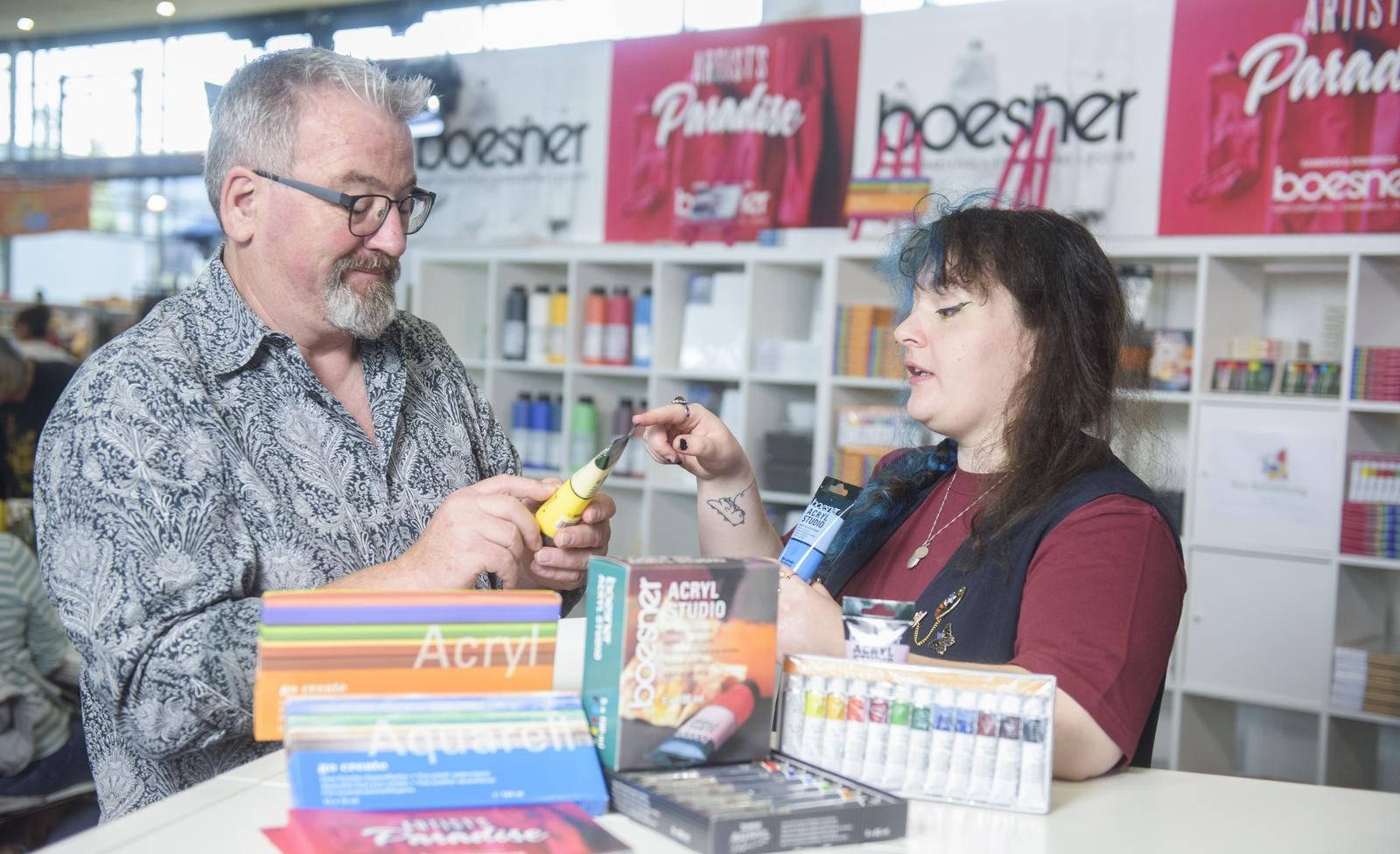Ein Besucher lässt sich Farben von einer Standmitarbeiterin auf der infa kreativ erklären